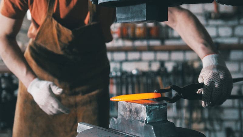 Bladesmith working a glowing billet under a power hammer